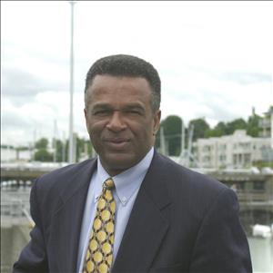 A Black man smiles into the camera with boats in the background