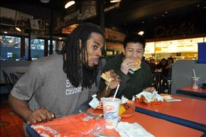 A black man and an asian man sitting in a restaurant eating hamburgers