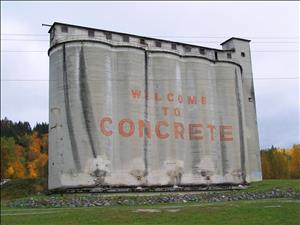 Large concrete structure consisting of 5 joined silos with a single-story building running along their roofs; "Welcome to Concrete" painted across silos
