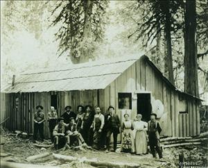 10 men, 2 women, and a little girl standing and sitting in front of small wooden building at Dillard's Bolt Camp
