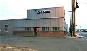 Photo of the building at First Avenue S and S Spokane Street in Seattle that housed The Dutchman Restaurant and later The Dutchman rehearsing and recording studio. It has a roman-brick exterior wainscoting under what appears to be vertical aluminum siding. A sign near the top of the second story reads "The Dutchman," dating back to its days as a restaurant.