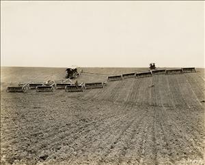 Two tractors driving up sloping plowed field with line of drills behind them