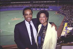 Photograph of Norm Rice with wife, Constance, at Seattle Mariners baseball game, with ball field behind and below and stands filled with people.