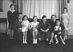 Family of eight posing on couch in front of large curtain in semi-formal clothes
