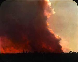 Giant plume of red smoke rising from a wooded horizon