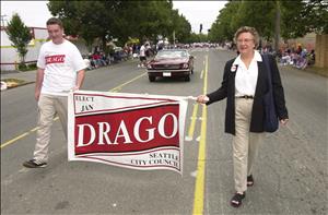 Two people walk down the middle of a road carrying a banner that says Elect Jan Drago Seattle City Council