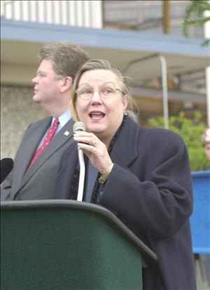 A woman in a winter coat speaks into a microphone at a podium. 