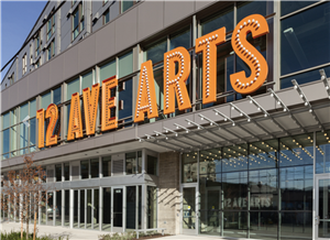 A modern building with lots of windows and a bright orange sign that says 12th Avenue Arts