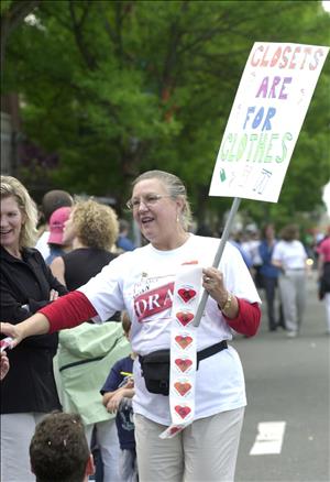 A woman carrying a sign that says Closets are for Clothes hands out heart shaped stickers. 