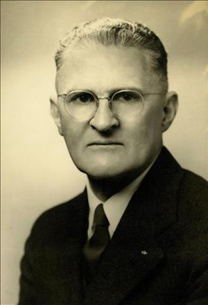 A head and shoulders portrait of a serious man with glasses. 