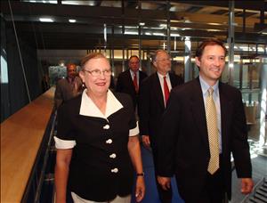 People in dress clothes walk down a glass lined hallway. 