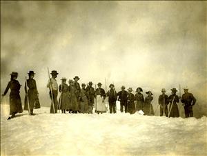 Men and women in early 20th century hiking clothes stand on a snowy bluff