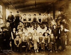 Four rows of men face the camera wearing work clothes and hats.