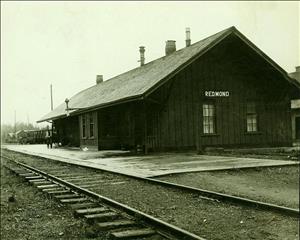 A one story wooden building next to railroad tracks with a sign that says Redmond.