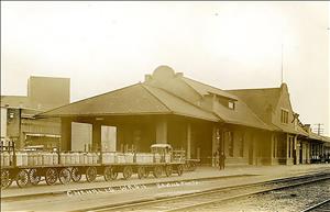 A one story building next to railroad tracks with porter wagons parked in front.