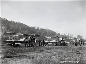 Three single propellor biplanes parked in a grassy field with people standing on and around them. 