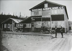 A two story wooden workshop with two model t cars parked in front. On the building the words Boeing Airplane Co are painted. 