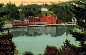 Red brick factory buildings along the shore of a tree lined lake. A large white mansion on the hill in the distance. 