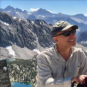 A smiling man with snow capped peaks behind him