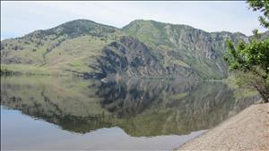 A forested hill is reflected in a large lake