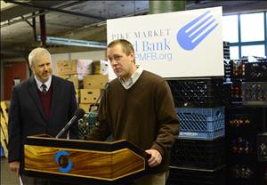 Two white men at a podium with grocery crates and boxes stacked behind them