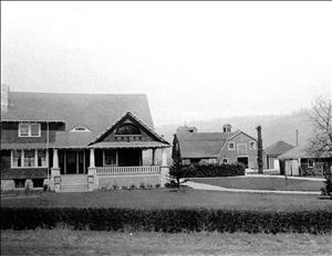 A large farmhouse with a wrap around porch and a barn in the background. 