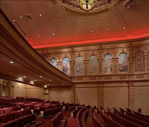 Rows of red theater seats beneath a domed ceiling, a balcony, and a row of panels painted to depict old venice. 