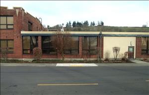 A one story brick building next to a two story brick building, with a two way street in front. 