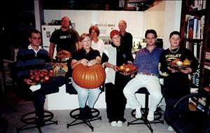 People of various ages pose for the camera holding pumpkins and fruits. 