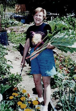 A woman stands in a vegetable garden smiling and holding large greens perhaps chard or kale. 