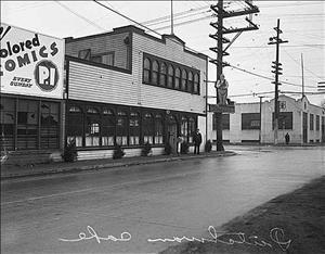 The Dutchman Restaurant in south Seattle in 1936. It will be the future home of The Dutchman rehearsing and recording studio. On the far right corner of the building a sign extends over the street featuring a male human figure, presumably a Dutchman. Painted on the wall to the left is an advertisement for the Seattle P-I boasting of "colored comics every Sunday."