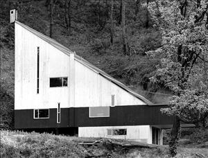 A triangular concrete house on a hill surrounded by trees. 