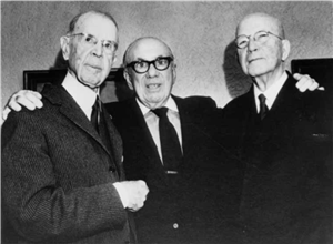Three elderly white men in suits and ties with eyeglasses. The one in the middle has his hands on the shoulders of the other two. 
