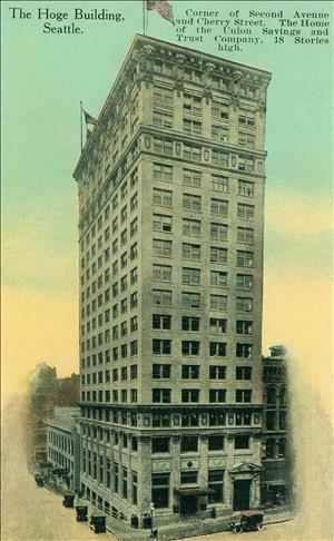 A postcard depicting an eighteen story stone building at the intersection of two city streets. 