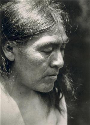 A bare chested indigenous man with long dark hair.
