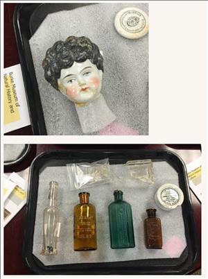 A porcelain dolls head and antique bottles rest on layers of foam in shallow trays