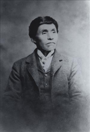 Portrait of an indigenous man in a suit coat, vest, and cravat looking off to his left.