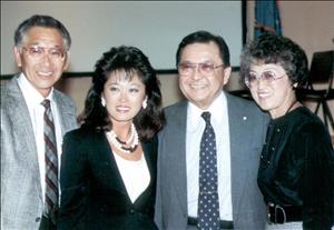 Two Asian men in suits and ties pose with their arms around two Asian women.