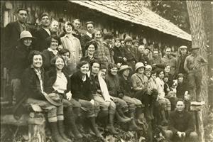 Three rows of young people standing and sitting in front of a rustic wooden cabin. 