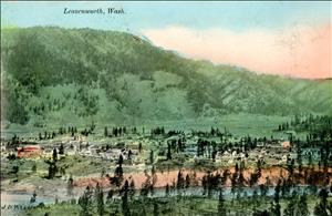 A green valley with small dotted trees houses, has a river running through it. Green mountains in the background are covered with trees with trees, and the sun is setting.