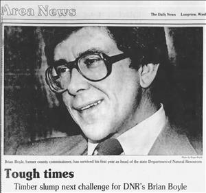 A newspaper clipping of a smiling man in large eyeglasses and a tie above text that says Tough Times. Timber Slump Next Challenge for DNR's Brian Boyle. 