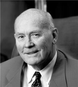A head and shoulders portrait of a smiling bald man in a suit and tie. 