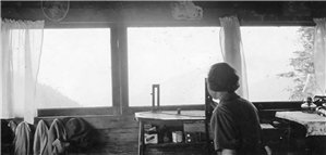 A woman sits in front of a round, metal piece of equipment and looks out a row of windows.