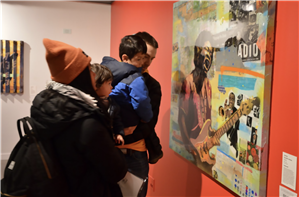 Two Asian adults each holding a child look at a painting on an orange wall