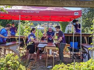 Seven young people in purple tie dye shirts play marimbas under a red canopy in a garden