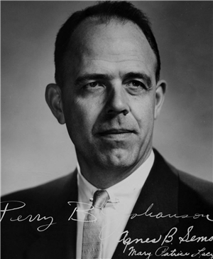 Head and shoulders portrait of a white man in a white shirt and tie. 