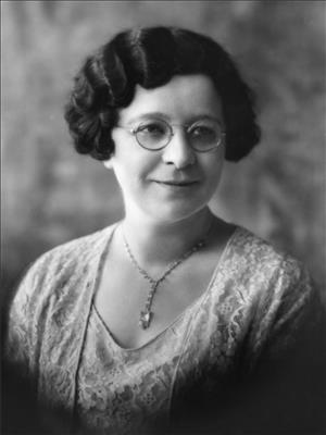 Head and shoulders portrait of a woman with curly hair wearing glasses and a lace dress.