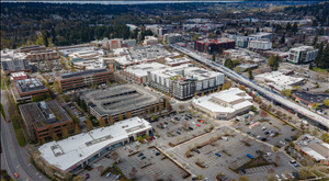 Birds eye view of modern office buildings and parking lots on either side of a highway. Forested hillsides in the background. 