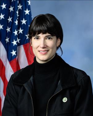 Head and shoulders portrait of woman with black hair in front of U.S. flag