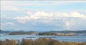 View from high point overlooking tops of trees and across a water channel with a few small islets in it to a number of larger islands in the background, mostly tree-covered with rolling hills 